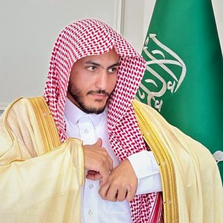 Salem Khalaf Al Shammari in a bisht, beside the flag of Saudi Arabia